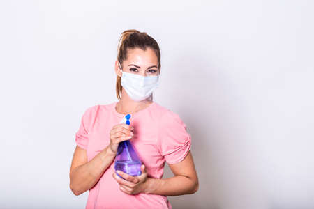 Woman with protective facial mask and disinfectant spray bottle . She sprinkling disinfectant and...