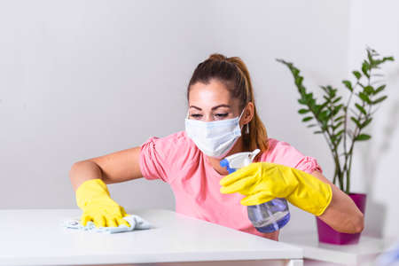 Woman with protective glove and facial mask doing housework, housewife portrait. She sprinkling...