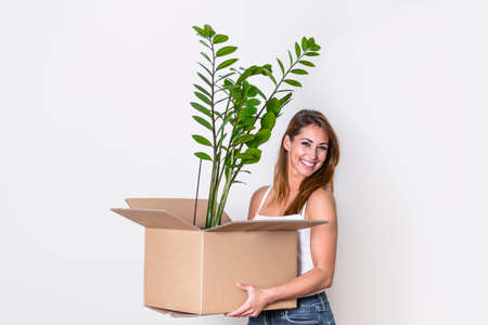 The young happy woman is moving into a new house. She brings a box with her favorite plant to her new home.の写真素材