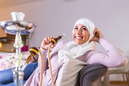 Muslim woman smoking shisha at home. Muslim young woman enjoying while smoking nargile. Arab girl smoking Hookahの写真素材