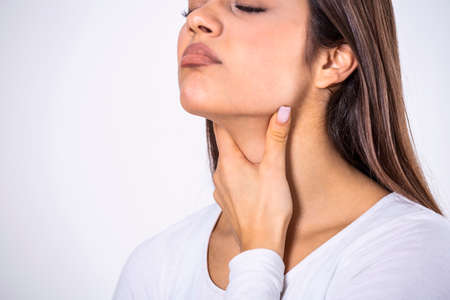 Young beautiful woman suffering from pain in throat, touching inflamed zone on her neck, cropped, empty space, sore throatの写真素材