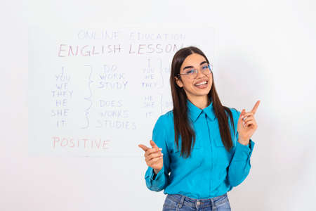 Modern education remotely. Cheerful young woman points to blackboard and explains rules of english onlineの写真素材