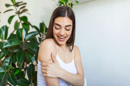 Woman pointing at his arm with a bandage after receiving the covid-19 vaccine. Young woman showing her shoulder after getting coronavirus vaccineの写真素材