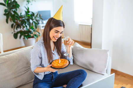 New normal concept. Happy woman celebrating her birthday alone. young woman holding a cake. Birthday party at home. Family video call. Social distancing. Life at home.の写真素材