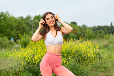 Young woman runner listening to music on earphones. Fit sportswoman taking a break from outdoors training. Woman Listening Music, Doing Workout Exercises On Street.の写真素材