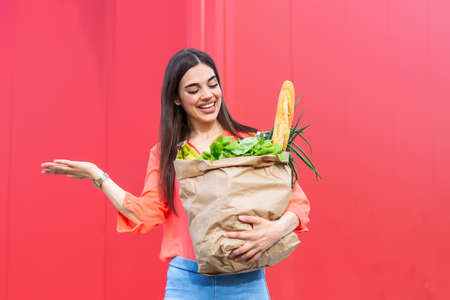 young woman holding a shopping bag full of vegetables groceries, Young woman holding grocery paper shopping bag full of fresh vegetables. Diet healthy eating conceptの写真素材