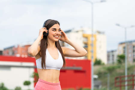 Young woman runner listening to music on earphones. Fit sportswoman taking a break from outdoors training. Woman Listening Music, Doing Workout Exercises On Street.の写真素材