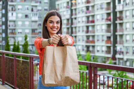 Woman delivering food in paper bag.Female volunteer holding groceries in the house porch. Delivery food service at home. Courier delivered the order no name bag with food.の写真素材
