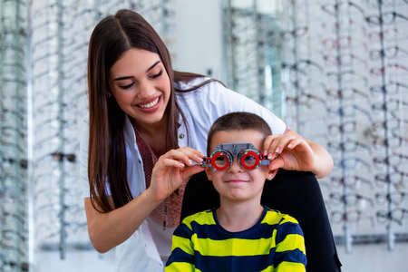 Attractive ophthalmologist examining youg boy with optometrist trial frame. Kid patient to check vision in ophthalmological clinic.の写真素材
