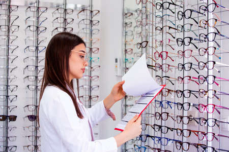 Attractive female ophthalmologist writing data to a clipboard, working in an optical store....