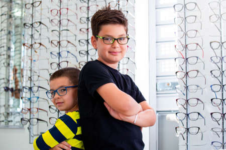 Health care, eyesight and vision concept - two boys choosing glasses at optics store.の写真素材