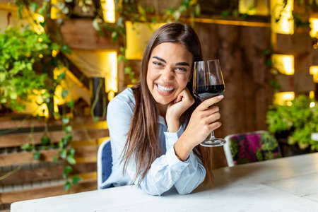 Image of cute pretty young woman sitting in cafe holding glass and drinking wine. portrait of a beautiful wine tasting tourist woman.の写真素材