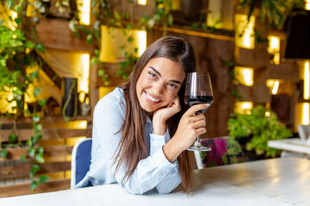 Image of cute pretty young woman sitting in cafe holding glass and drinking wine. portrait of a beautiful wine tasting tourist woman.の写真素材