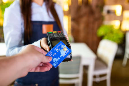 Contactless payment concept, female holding credit card near nfc technology on counter, client make transaction pay bill on terminal rfid cashier machine in restaurant store, close up viewの素材 [FY310189928852]