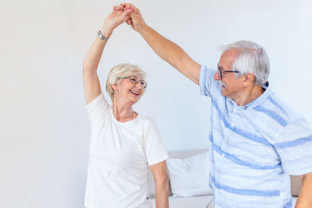 Joyful active old retired romantic couple dancing laughing in living room, happy middle aged wife...