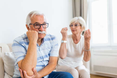 Senior couple arguing. Elderly woman frustrated with her husband. Older couple sitting on the sofa at home,having fight. Marriage issues, pre-divorce periodの写真素材