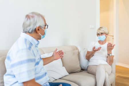 Senior friends having conversation on the sofa at home during Covid 19 pandemic. Elderly wearing...