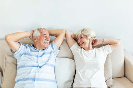 Calm senior mature couple relaxing on soft comfortable sofa having daytime nap together, carefree middle aged old family breathing fresh air enjoying no stress free peaceful weekend resting on couchの写真素材