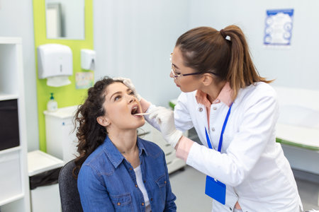 Doctor using inspection spatula to examine patient throat. ENT doctor doing throat exam of a woman. patient opened her mouth to throat check-upの写真素材