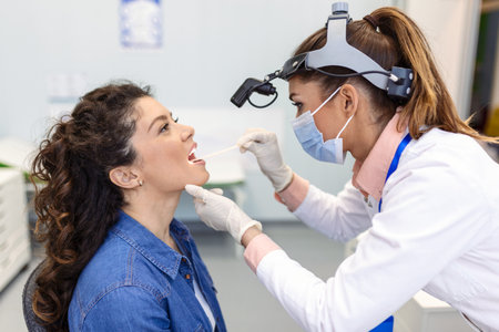 Doctor using inspection spatula to examine patient throat. ENT doctor doing throat exam of a woman. patient opened her mouth to throat check-upの写真素材