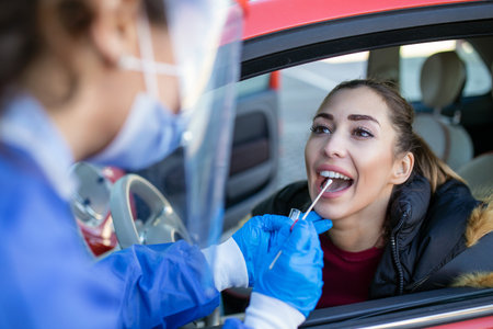 Medical worker performing drive-thru COVID-19 check,taking nasal swab specimen sample from female...
