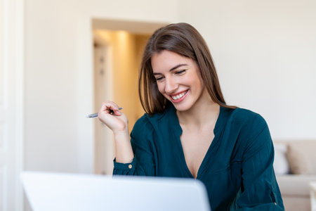 Portrait of a smiling young woman working on laptop computer at homeの写真素材
