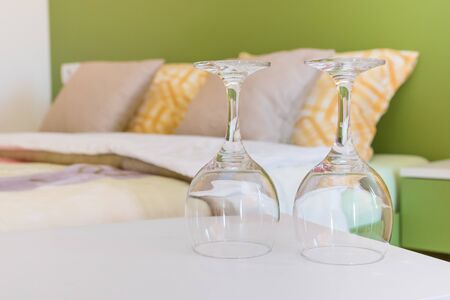 Two empty wine glasses turned upside down on night table next to the double bed in modern hotel bedroom. Valentines day or anniversary concept. Close up.の写真素材