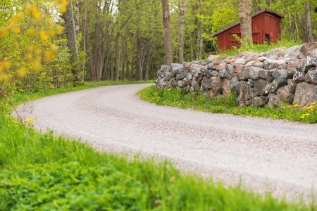 Side of a countryroad with a stonewall and a red house in Sweden during summerの写真素材