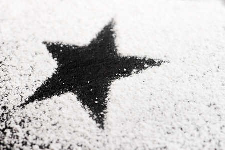 Black star made of white powdered sugar on a black granite plateの写真素材