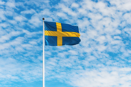 Swedish flag waving in wind against a blue sky with light white clouds, horizontalの写真素材
