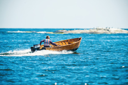 GRISSLEHAMN, NORRTALJE - JULY 11: Man with a fast vintage wooden speedboat at coast of Sweden. July 11, 2014 in Grisslehamn, Sweden.のeditorial素材