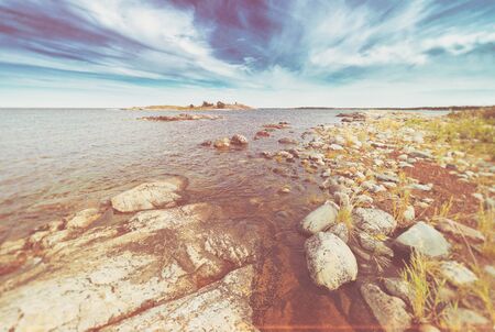 Coastal scene with vegetation on the round rocks at seafront during summer. Filters appliedのeditorial素材