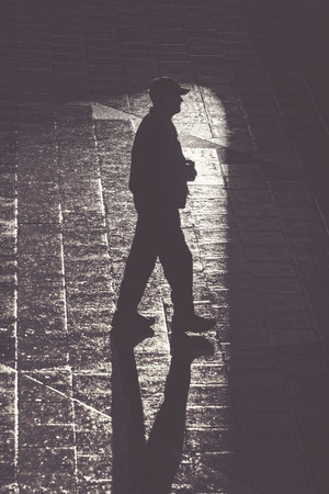 Walking man with long shadows in high contrast, filter appliedの写真素材