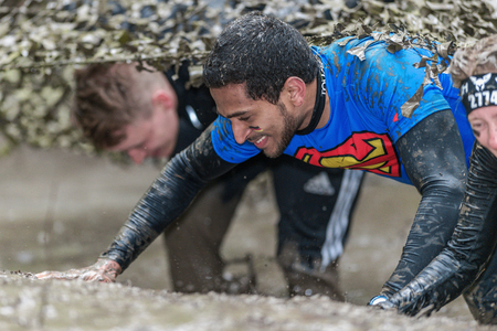 STOCKHOLM, SWEDEN - MAY 14, 2016 Crawling under the muddy net trap in Tough Viking obstacle course...