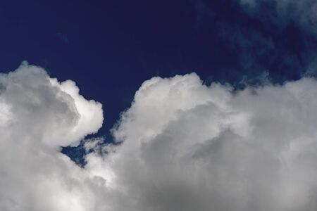 Cloudscape with white cumulus clouds with dark blue sky during daytime.