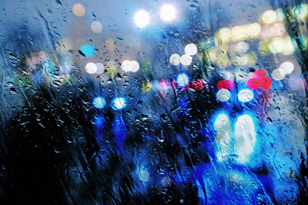 Wet window of defocused colorful lights and reflections from the wet street.