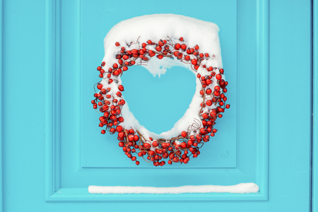Wreath in red rowan berries on the cyan front door covered in snow, heart shaped. Norway, abstractの写真素材