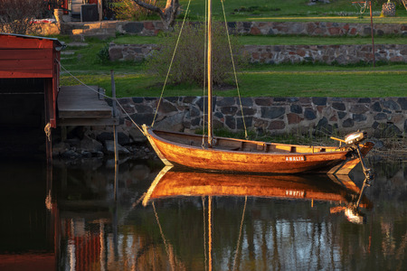 GRISSLEHAMN, SWEDEN, MAY 12, 2018: Vintage wooden boat anchored in the eveningsun at a boathouse, great reflections in the calm water.のeditorial素材
