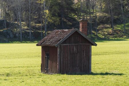 Abandoned wooden storage barn in red worn colors in a green cropfield with forest in the background. Summer and colorfulの写真素材
