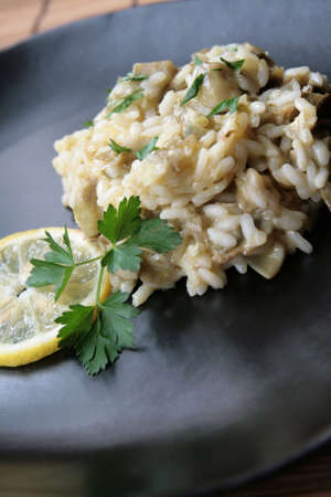Close-up of a dish of risotto with artichokes in a black plate, decorated with parsley and a slice of lemonの写真素材