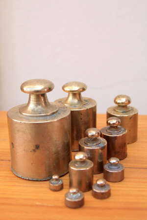 Antique weights from an old scale, made of brass, on a wooden surface and with a light backgroundの写真素材