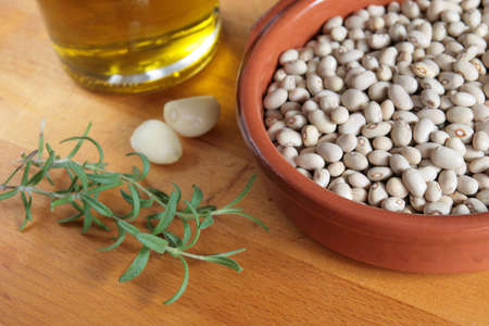 A bowl of raw beans, with olive oil, garlic and fresh rosemary on a wooden boardの写真素材