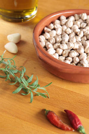 A bowl of raw chickpeas, with olive oil, garlic, chilli peppers and fresh rosemary on a wooden boardの写真素材