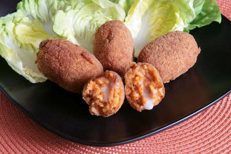 Roman rice croquettes filled with tomato sauce and mozzarella, on a bed of lettuce in a black plateの写真素材