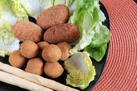 Mixed plate of fried appetizers: roman rice croquettes filled with tomato sauce and mozzarella, and fried olives typical of Marche region filled with meat, on a bed of lettuce in a black plateの写真素材
