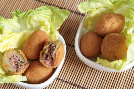 Fried olives typical of Marche region filled with meat, on a bed of lettuce in two whites bowlsの写真素材