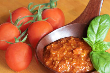 Bolognese meat sauce in a wooden spoon with tomatoes on a wooden boardの写真素材