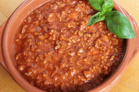 Bolognese meat sauce in an earthenware bowl on a wooden boardの写真素材