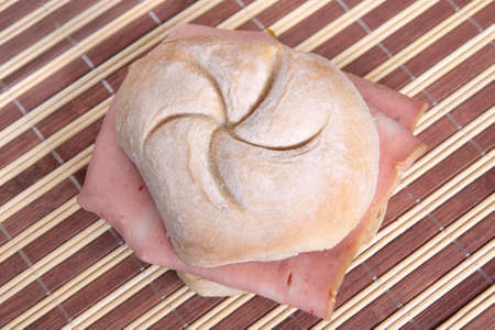 Bread roll filled with Bologna on a bamboo place matの写真素材