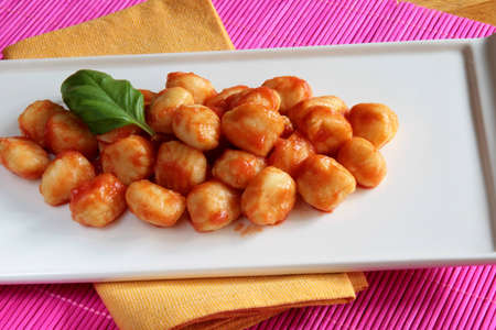 Plate of tomato sauce gnocchi on yellow napkin and pink place matの写真素材